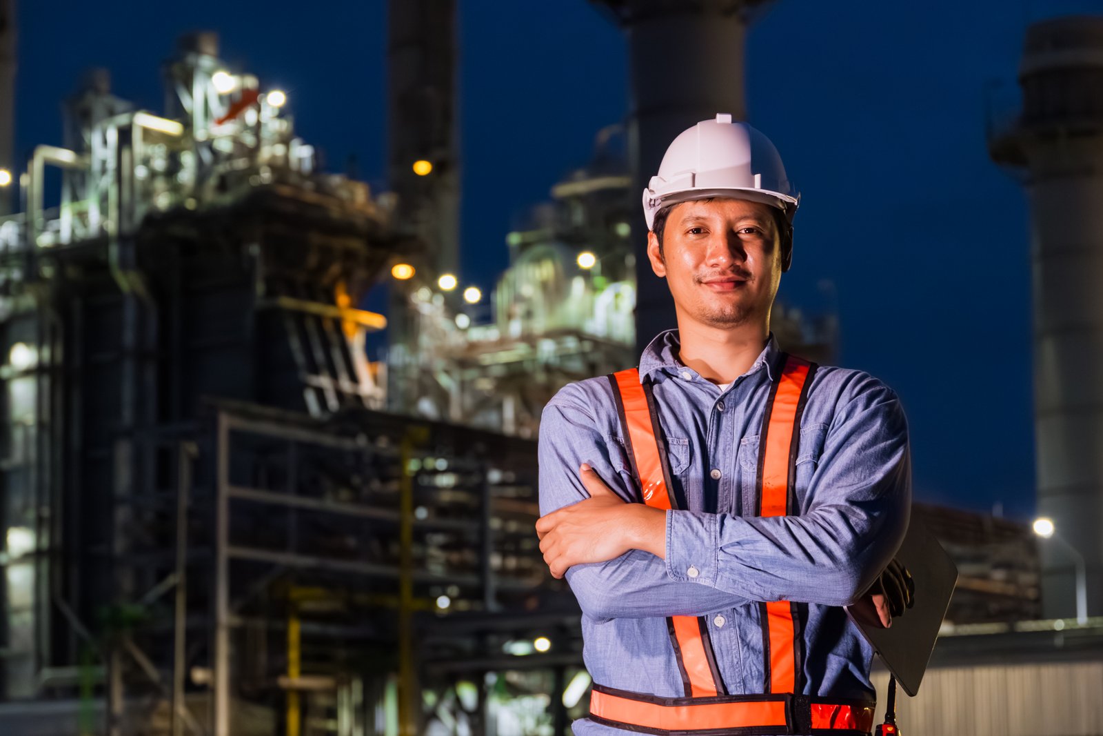 Engineer professional Asian male standing confident happy against Petroleum Refinery industry at Night. Oil and Gas Petrochemical Power plant business leader.