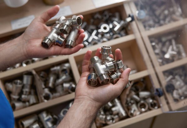 Male plumber holding steel adapters for plumbing with external thread. High angle closeup view on hands with variety of fitting accessories. Shop assortment